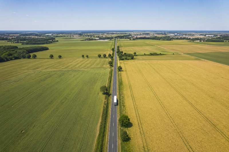 Camion de déménagement seul sur une route traversant des champs cultivés