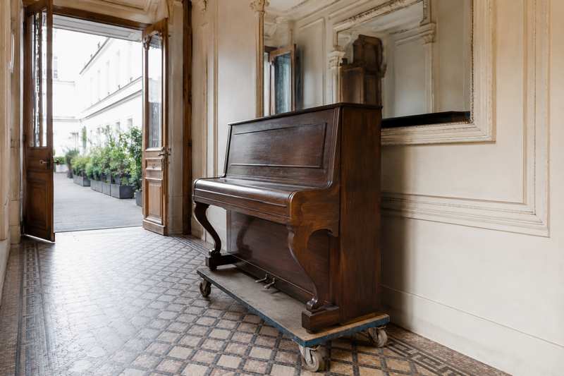 Piano droit sanglé sur un chariot dans l'entrée d'un immeuble ancien